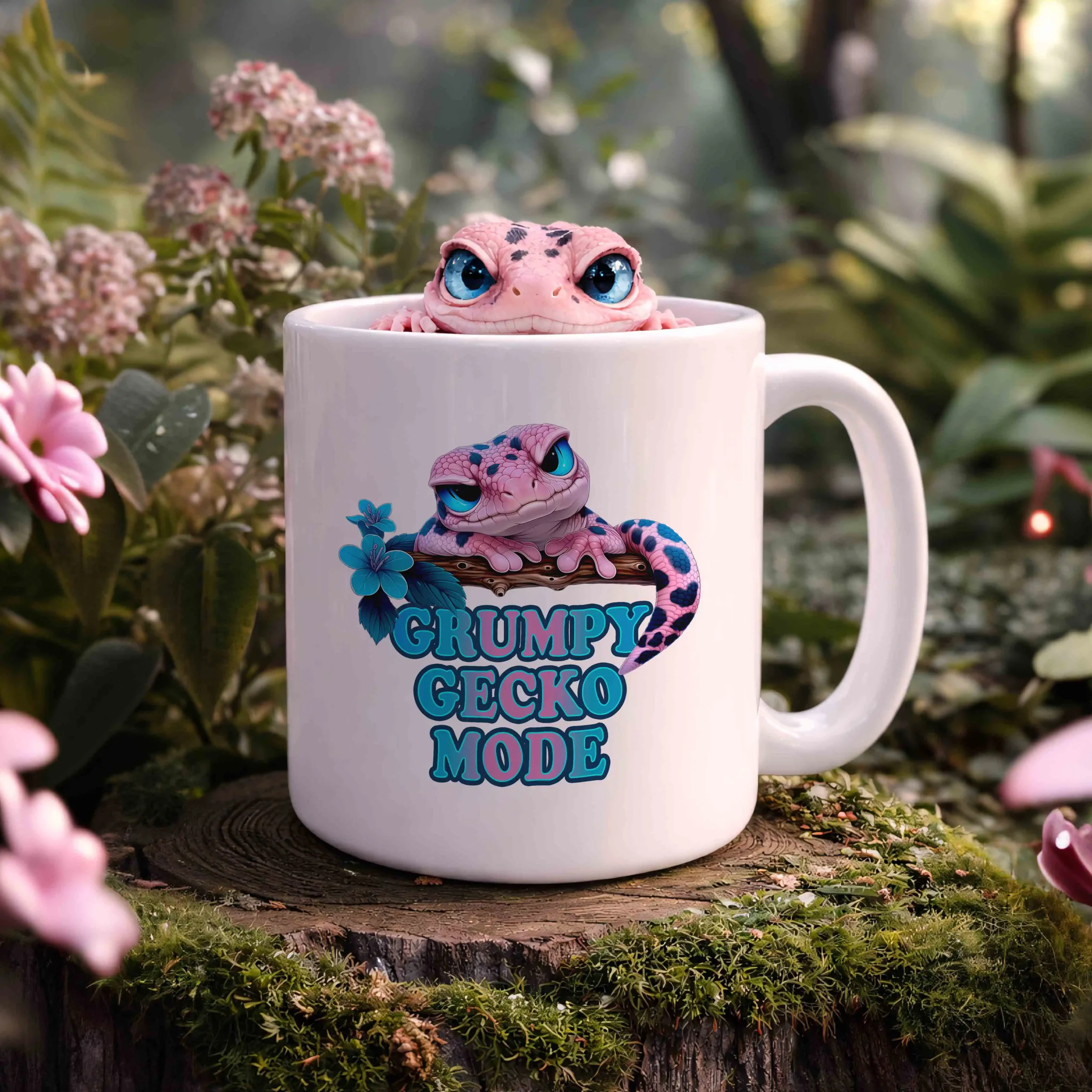 Weiße Tasse mit „Grumpy Gecko Mode“-Motiv und süßem Gecko, platziert auf einem Baumstumpf in natürlicher Umgebung mit Blumen und weichem Hintergrund